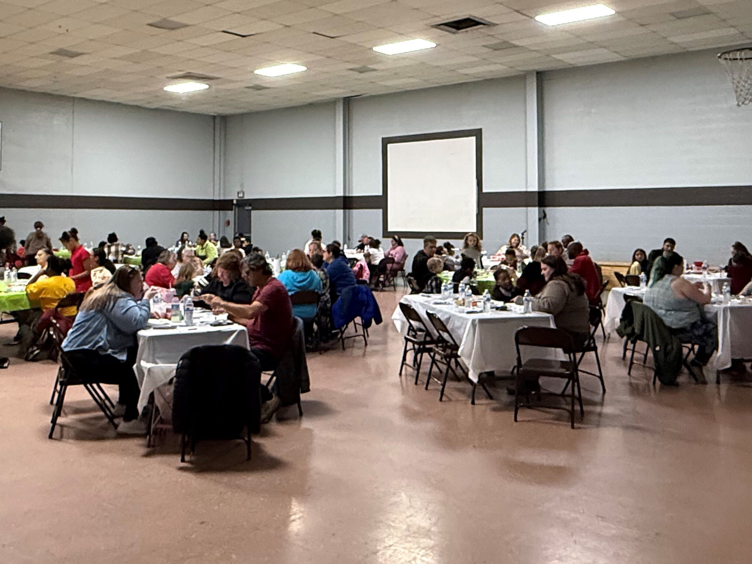 Room full of people, sitting at tables, sharing a meal and talking. 