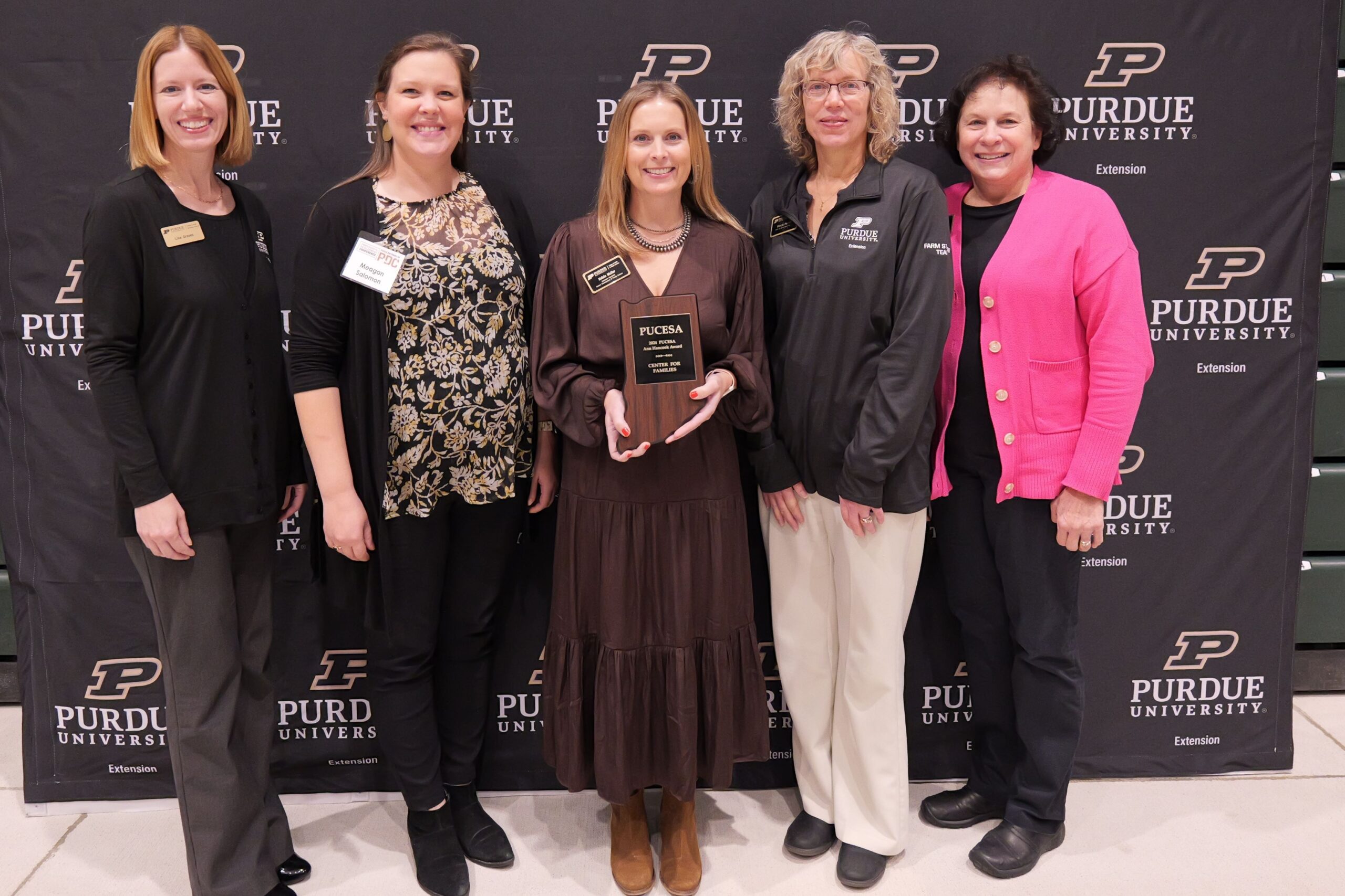 five people facing the camera. person in the middle holding a plaque